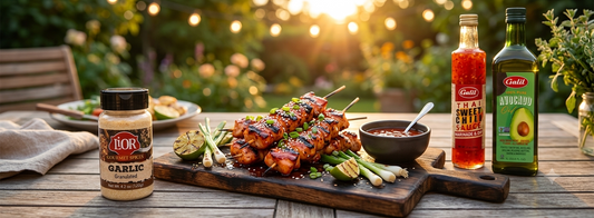 Grilled sweet chili chicken skewers served with scallions and lime alongside Lior garlic seasoning, Galil sweet chili sauce, and avocado oil.